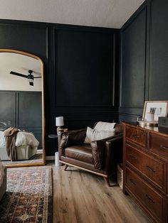 a living room with black walls and wood floors, a leather chair in front of a large mirror