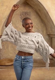 a woman standing in front of a stone wall with her arms up and smiling at the camera