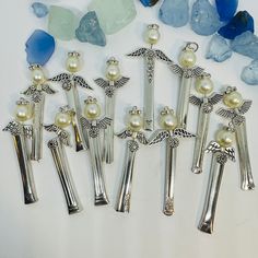 seven silver pins with pearls and angel wings on them next to some sea glass pieces