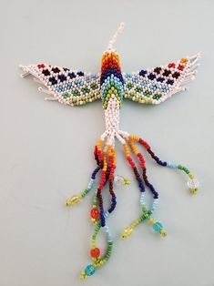 a bird made out of beads on a white surface with one wing extended and the other wings down