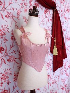 A pair of Balletcore Renaissance, Baroque, Rococo, Regency, Victorian Era Corset Stays in Ballet Pastel Pink with Rosette Appliques in front of a toile backdrop. Elegant Fitted Pink Corset, Feminine Fitted Pink Corset, Pink Feminine Underbust Corset, Pink Underbust Feminine Corset, Feminine Pink Underbust Corset, Pink Feminine Corset With Boned Bodice, Pink Fitted Wedding Corset, Fitted Pink Wedding Corset, Elegant Fitted Pink Bodice