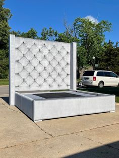 a white bed sitting on top of a cement slab next to a parking lot with a car parked in the background