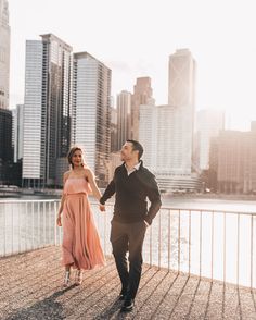 a man and woman are holding hands while walking in front of the cityscape