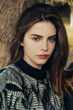 a beautiful young woman standing next to a tree