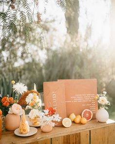 a table topped with oranges and flowers on top of a wooden table next to a sign