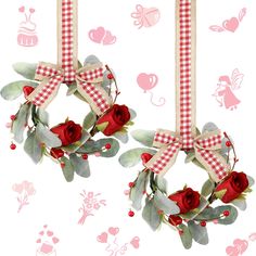 two wreaths with red roses and green leaves hanging from strings on a white background