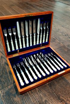 an open wooden box filled with silverware on top of a wooden floor next to a knife and fork