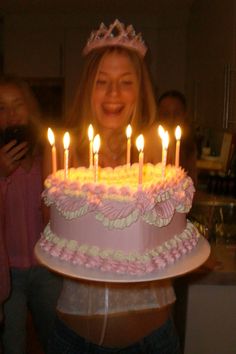 a woman holding a birthday cake with lit candles on it in front of her face