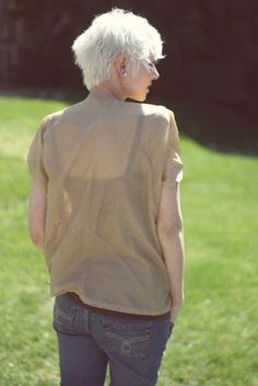 an older woman standing in the grass with her back to the camera, looking at something