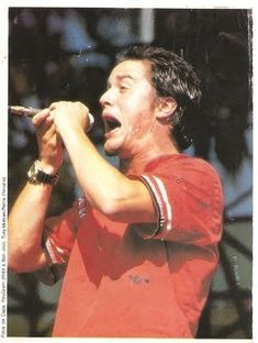 a man singing into a microphone with his hands in the air while wearing a red shirt