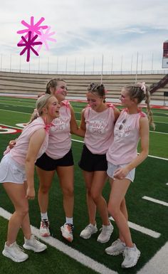 four girls in pink shirts and black shorts standing on a football field with their arms around each other