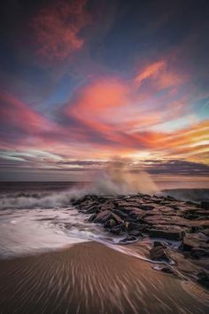 the sun is setting at the beach with waves crashing in front of rocks and water