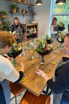 a group of people standing around a wooden table with flowers in vases on it