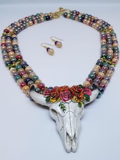 "Colors of the desert highlight this 3-strand necklace and matching earrings. The glass beads look like Indian corn. The cow skull pendant is cast resin. The necklace features a hand-made 3-strand hook-and-eye clasp. The spacer bars, wire, and earwires are gold plated. The earrings are 1.25\" long. This set would go great with jeans and a blazer, or more formal wear. Let's dream of the desert tonight!" Cow Skull Necklace, Dream Necklace, Peace Earrings, Indian Corn, Desert Dream, Bead Bar, The Cow, Cow Skull, Skull Necklace