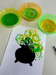 some green and yellow paint sitting on top of a white paper next to two bowls