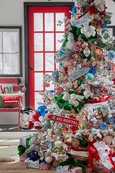 a decorated christmas tree in front of a red door with gifts around it and ribbon on the top