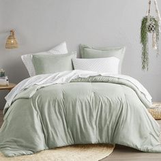 a bed with green comforter and pillows in a room next to a rug on the floor