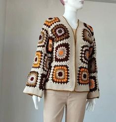 a white mannequin wearing a crocheted jacket and beige pants with an orange, brown, and yellow design on it