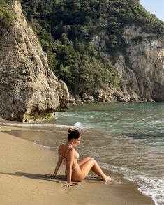 a woman is sitting on the beach by the water