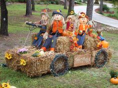 three scarecrows are riding in a hay cart with pumpkins and flowers on it