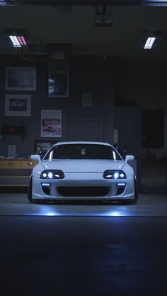 a white sports car parked in a garage at night with its lights on and the hood up