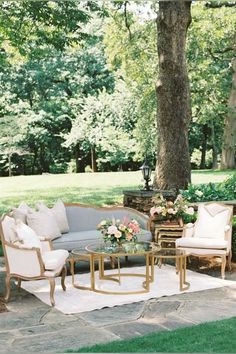 an outdoor seating area with couches, tables and chairs in the grass near a tree