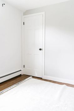 an empty room with a white door and hard wood flooring on the side wall