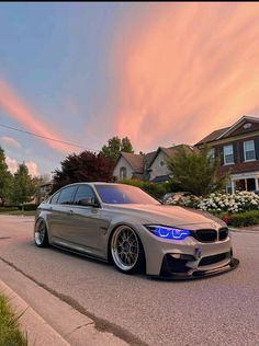 a silver car is parked on the street in front of some houses and trees at sunset