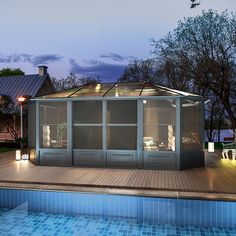 a gazebo next to a swimming pool at night with lights on the roof and windows