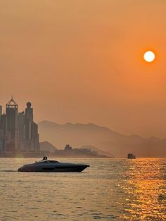 the sun is setting in front of a large city and water with boats on it