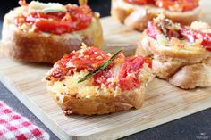 small pieces of bread with tomatoes and herbs on them sitting on a wooden cutting board