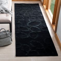 a black rug on the floor next to a chair and handbag in front of a window