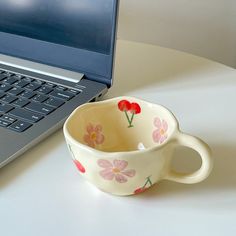 a coffee cup sitting in front of a laptop computer on a white table with flowers painted on it