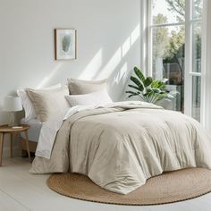 a bedroom with white walls and flooring has a large bed covered in beige linens