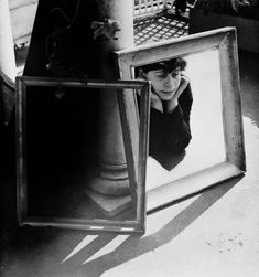 a black and white photo of a woman looking at her reflection in a framed mirror