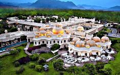 an aerial view of a large building in the middle of a lush green area with mountains in the background