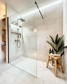 a walk in shower sitting inside of a bathroom next to a wooden stool and potted plant