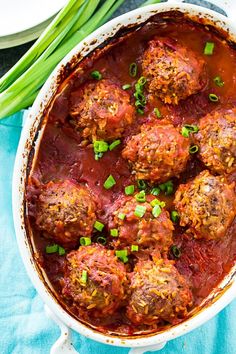 meatballs covered in marinara sauce and garnished with scallions on a blue cloth