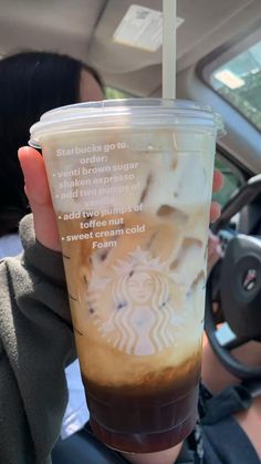 a person holding up a cup of coffee in the back seat of a car while driving