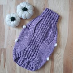 a purple knitted mitt and two white pom - poms on a wooden floor