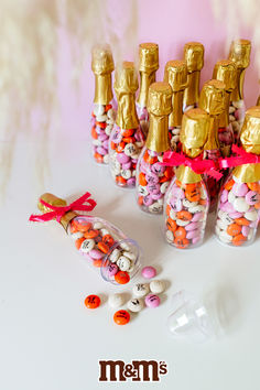 there are many candy in the bottles with gold caps on them and pink ribbons tied to each bottle