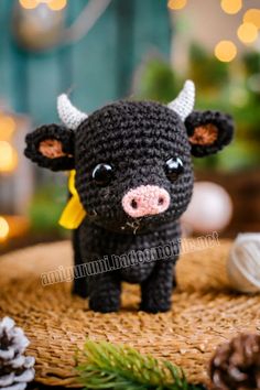 a small crocheted black cow sitting on top of a table next to pine cones