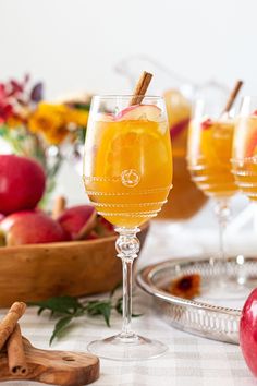 two glasses filled with apple cider on top of a table next to apples and cinnamon sticks