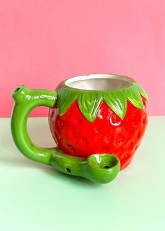 a green and red ceramic strawberry mug on a white table next to a pink wall