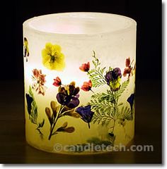 a glass candle holder with flowers painted on it's sides and the light turned on