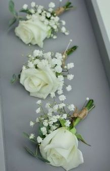 three white roses and baby's breath are arranged in a row on a gray surface