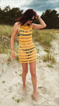 a woman standing on top of a sandy beach next to grass and sand covered ground