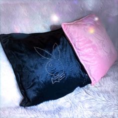 two black and pink pillows sitting on top of a white fur covered floor next to each other