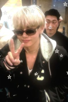 a woman in sunglasses making the peace sign with her hand while another man looks on