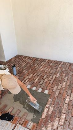 a man laying bricks on the ground with a paint can and brush in his hand